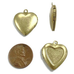 May include: A set of four antique brass-colored heart-shaped lockets. The lockets are shown from multiple angles, including a side view and an open locket. A penny is included for size comparison. The lockets have a loop at the top for a chain.