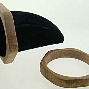 Könnte beinhalten: Zwei Holz-Armbänder, eines ist quadratisch und das andere rund. Beide Armbänder sind aus hellbraunem Holz.