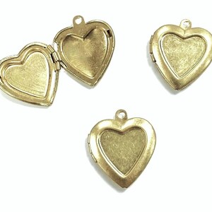 May include: Three antique gold-colored heart-shaped lockets. One locket is open, revealing the interior. Each locket has a small loop at the top for attaching to a chain. The lockets are on a white background.