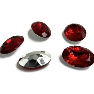 Könnte beinhalten: Fünf ovale Edelsteine. Vier sind tiefrot, einer silberfarben. Die Steine sind facettiert und reflektieren das Licht. Sie liegen auf einem weißen Hintergrund. Geeignet für Schmuck.