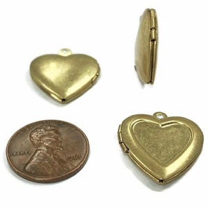 May include: A collection of antique brass heart-shaped lockets. The lockets are shown from multiple angles, including an open locket and a side view. A penny is included for size reference. The lockets have a loop for a chain.