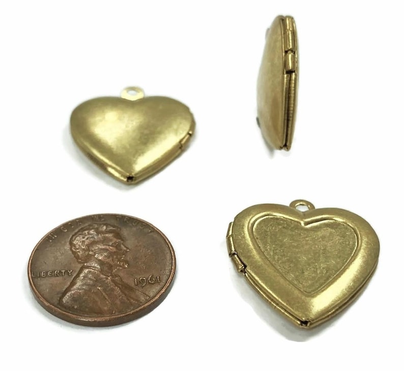 May include: A collection of antique brass heart-shaped lockets. The lockets are shown from multiple angles, including an open locket and a side view. A penny is included for size reference. The lockets have a loop for a chain.