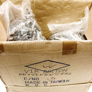 May include: A cardboard box with a brown and white label that reads "WIR BOSTON PROVIDENCE RI C/NO. MADE IN TAIWAN R.O.C.". The box is filled with two plastic bags containing silver metal hardware.