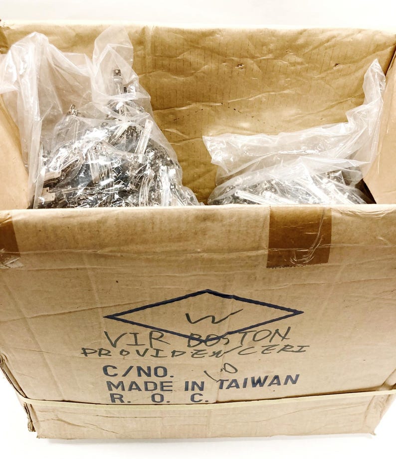 May include: A cardboard box with a brown and white label that reads "WIR BOSTON PROVIDENCE RI C/NO. MADE IN TAIWAN R.O.C.". The box is filled with two plastic bags containing silver metal hardware.