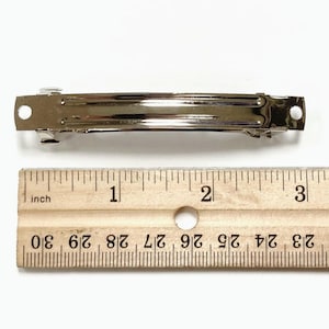 May include: A silver metal hair clip measuring 2 inches long. The clip is shown next to a ruler for size reference.