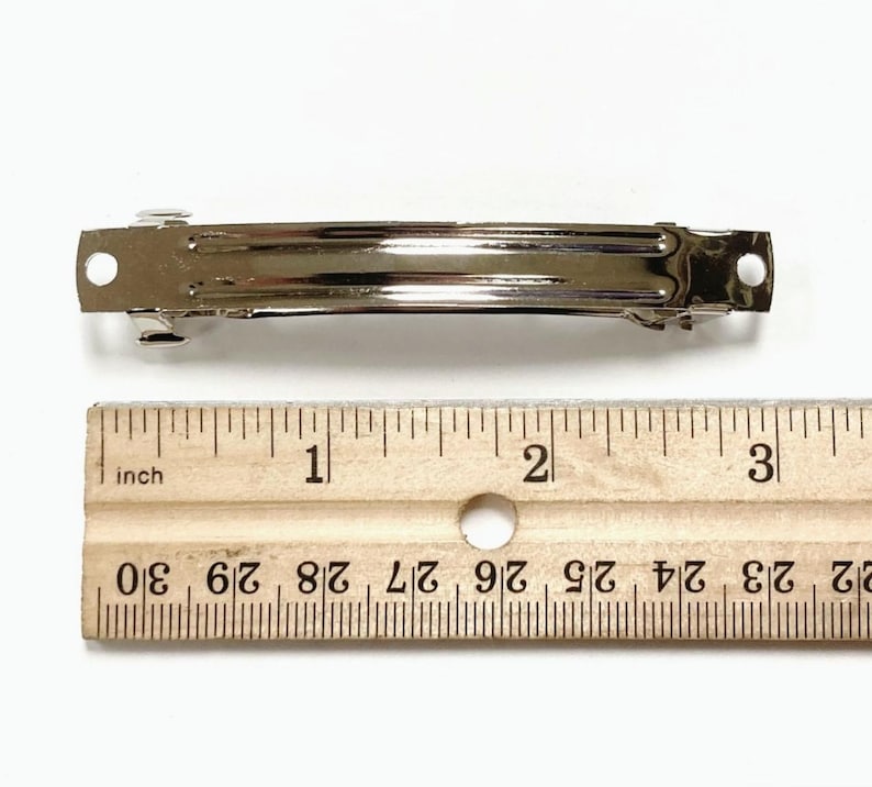 May include: A silver metal hair clip measuring 2 inches long. The clip is shown next to a ruler for size reference.