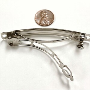 May include: A silver metal hair clip with a spring mechanism. The clip is about the size of a US penny.