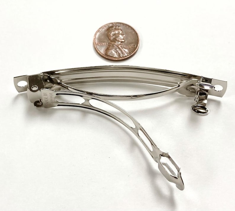 May include: A silver metal hair clip with a spring mechanism. The clip is about the size of a US penny.