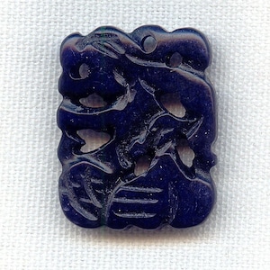 May include: A black jade pendant carved with an intricate design. The pendant has a hole at the top for hanging.