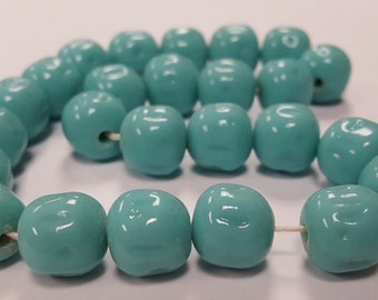 May include: A strand of turquoise blue glass beads. The beads are round and have a slightly irregular shape. The beads are strung on a white thread. The beads are approximately 1 cm in diameter. The beads are made in Japan.