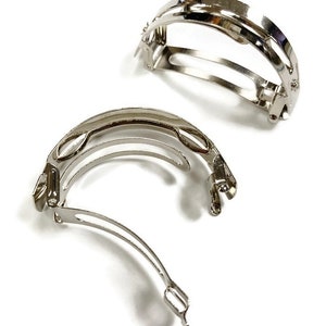 May include: Two silver metal hair clips with a curved design. The clips are open and ready to be used.