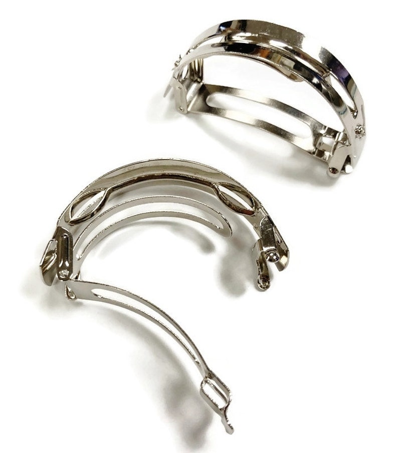 May include: Two silver metal hair clips with a curved design. The clips are open and ready to be used.