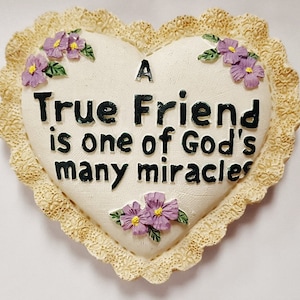 Può includere: Una placca bianca a forma di cuore con un bordo di pizzo e fiori viola. La placca recita "A True Friend is one of God's many miracles."