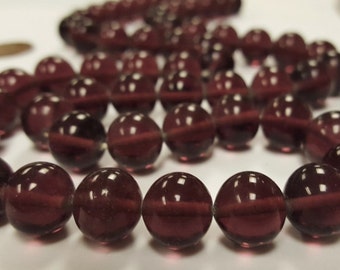 May include: A strand of deep purple glass beads. The beads are round and have a smooth, glossy finish.