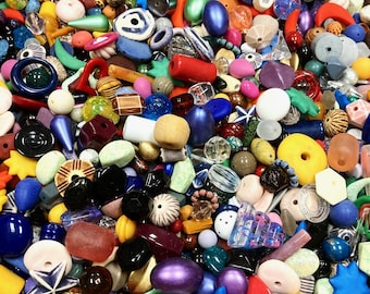 May include: A vibrant assortment of colorful beads in various shapes and sizes. The beads include a mix of materials and colors, such as red, blue, yellow, and purple. Some beads have unique textures and patterns, perfect for jewelry making or crafts.