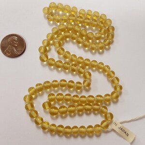 Puede incluir: Una hebra de cuentas de vidrio amarillo transl&uacute;cido. Las cuentas son redondas y tienen un ligero brillo. La hebra es lo suficientemente larga para hacer un collar o una pulsera. La etiqueta dice "IN JAPAN".