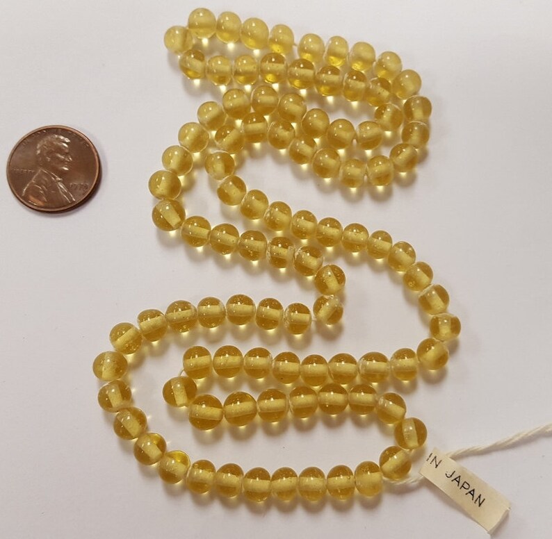 Puede incluir: Una hebra de cuentas de vidrio amarillo transl&uacute;cido. Las cuentas son redondas y tienen un ligero brillo. La hebra es lo suficientemente larga para hacer un collar o una pulsera. La etiqueta dice "IN JAPAN".