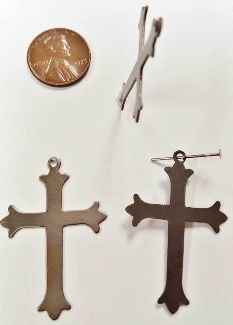 May include: Two silver-toned metal crosses with ornate details. The crosses are approximately the size of a US penny.
