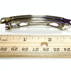 May include: A silver metal hair clip measuring 2 inches long. The clip has a simple design with a curved shape and a smooth finish.