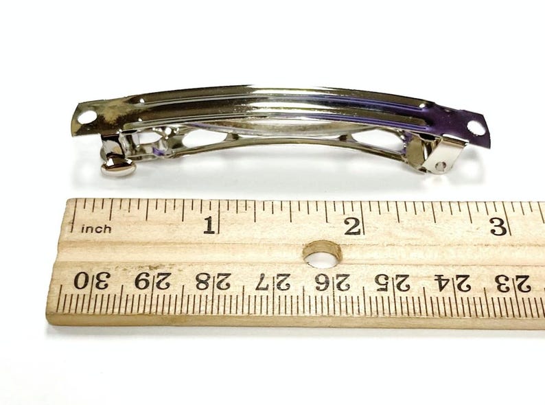 May include: A silver metal hair clip measuring 2 inches long. The clip has a simple design with a curved shape and a smooth finish.