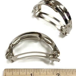 May include: Two silver metal hair clips, each measuring approximately 1 inch in length. The clips are designed to hold hair in place and have a curved shape.