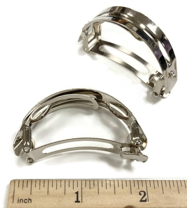 May include: Two silver metal hair clips, each measuring approximately 1 inch in length. The clips are designed to hold hair in place and have a curved shape.