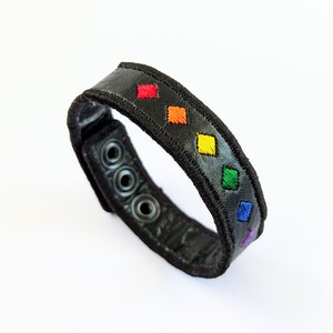 Puede incluir: Pulsera de cuero negro con un patrón de diamantes de arcoíris.
