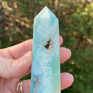 May include: A light blue and white crystal point with a natural, cloudy appearance. The crystal has a unique, swirling pattern and a small, red-brown inclusion.