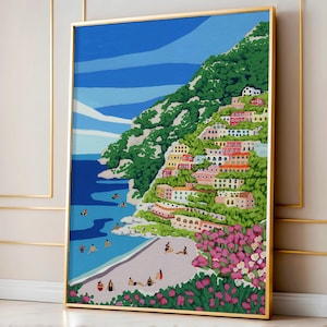 Beach art print with colorful flowers and bright houses and pink and green flowers on a mountainside hill with bright blue sky and little people on the shore and swimming in the bluey green water ocean sea. Calming and whimsical image of visitors to Positano village in Italy Europe. Gold Framed image of Positano leaning up against a Pink and Gold wall in European architecture interior building or home