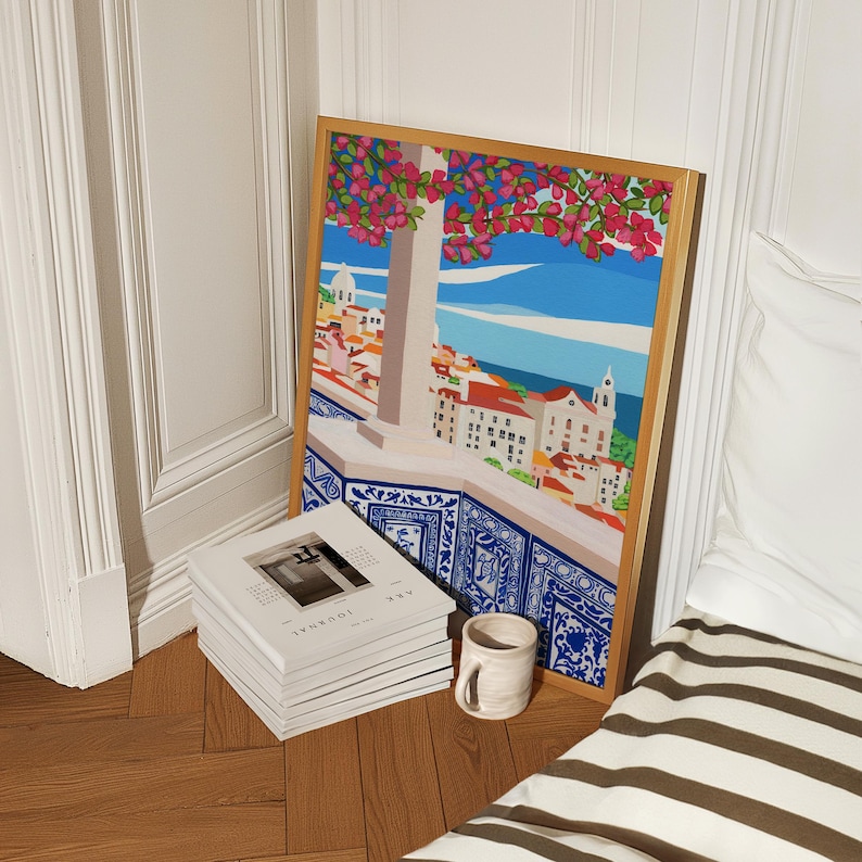 May include: A framed print of a colorful illustration depicting a cityscape with a blue sky, pink flowers, and a blue tiled balcony. The print is hanging on a white wall.