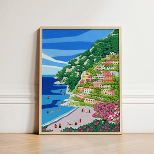 Beach art print with colorful flowers and bright houses and pink and green flowers on a mountainside hill with bright blue sky and little people on the shore and swimming in the bluey green water ocean sea. Calming and whimsical image of visitors to Positano village in Italy Europe. Neutral wooden soft light framed image of Positano up against a White decorative wall in European architecture interior building sitting on soft wooden herringbone floors