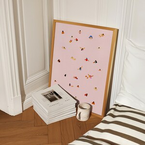 May include: A framed print of a pink background with small, colorful illustrations of people in various swimming positions. The print is leaning against a stack of white journals with the text "2022 JOURNAL" printed on the top journal.