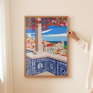 May include: A framed painting depicting a cityscape with a view of a blue ocean and a church with a white steeple. The painting features a balcony with blue and white patterned tiles and a pink flowering tree in the foreground.