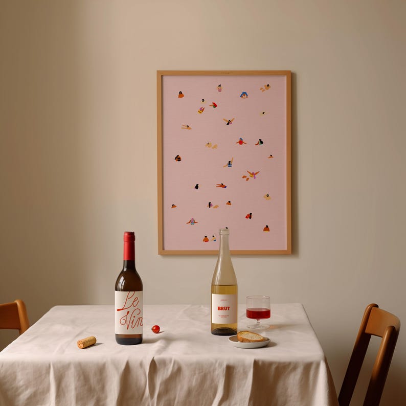 May include: A white tablecloth covers a table with two bottles of wine, one red and one white, a glass of red wine, and a piece of bread. A framed print of a pink background with small figures of people in various poses hangs on the wall behind the table.