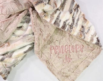 Puede incluir: Una manta suave y mullida con un patrón a rayas en tonos marrones, blancos y beige. La manta tiene un mensaje bordado personalizado que dice "Penelope Jo".