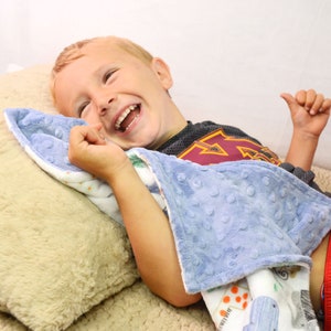 May include: A young boy is lying on a light brown pillow with a blue and white patterned blanket. He is laughing and has a red and black shirt on.