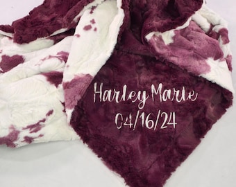 Puede incluir: Una manta suave y mullida con un diseño de estampado de vaca blanco y burdeos. La manta está personalizada con el nombre "Harley Marie" y la fecha "04/16/24" bordada en blanco.