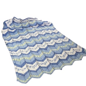 May include: A blue and white knitted baby blanket with a chevron pattern. The blanket has a scalloped edge.