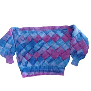 May include: A blue and pink knitted jumper with a woven pattern. The jumper has a wide neckline and long sleeves.