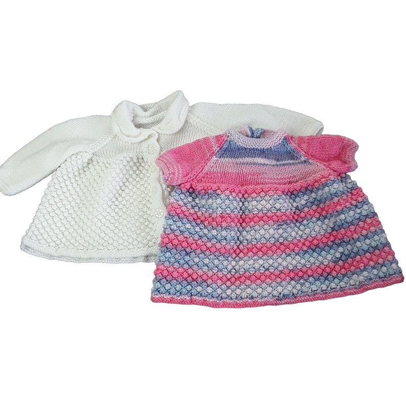 Hand knitted white baby cardigan and sparkly pink and blue dress on a white background