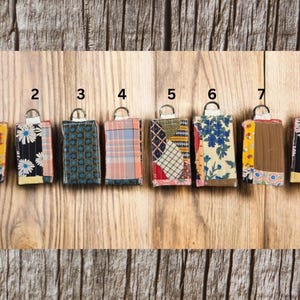 以下が含まれることがあります： 金属リングが付いた8つの布製キーホルダー。それぞれがユニークなパッチワークデザインです。キーホルダーは、黄色、青、赤などのさまざまな色で、花柄、チェック柄、幾何学模様など、さまざまなパターンが特徴です。