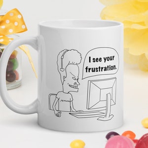 Op de afbeelding: Witte keramische mok met een zwarte lijntekening van een cartoonfiguur met stekelig haar dat een koptelefoon draagt en aan een computer zit. Het personage zegt "Ik zie je frustratie."
