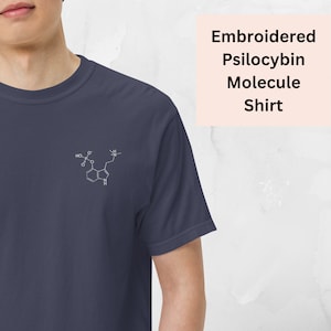 Peut inclure: Un t-shirt bleu marine avec un contour blanc brodé de la molécule de psilocybine. Le t-shirt porte le texte "Embroidered Psilocybin Molecule Shirt" dans un encadré rose.