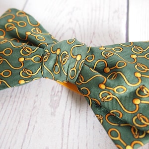 May include: A green bow tie with a gold chain pattern. The bow tie is tied and ready to wear.