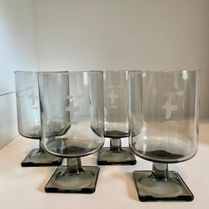 May include: Set of four gray glass tumblers with a square base and etched design. The glasses are clear with a smoky gray tint.