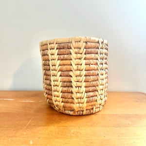 Könnte beinhalten: Ein geflochtener Korb in natürlicher Braun- und Beigetönung. Der Korb hat ein Chevron-Muster und ist aus natürlichen Materialien gefertigt.