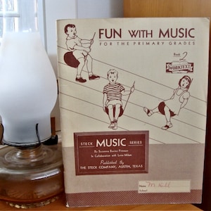 May include: A vintage book titled "Fun with Music" for primary grades, with a brown cover and illustrations of children playing music. The book is part of the Steck Music Series and is published by The Steck Company in Austin, Texas.