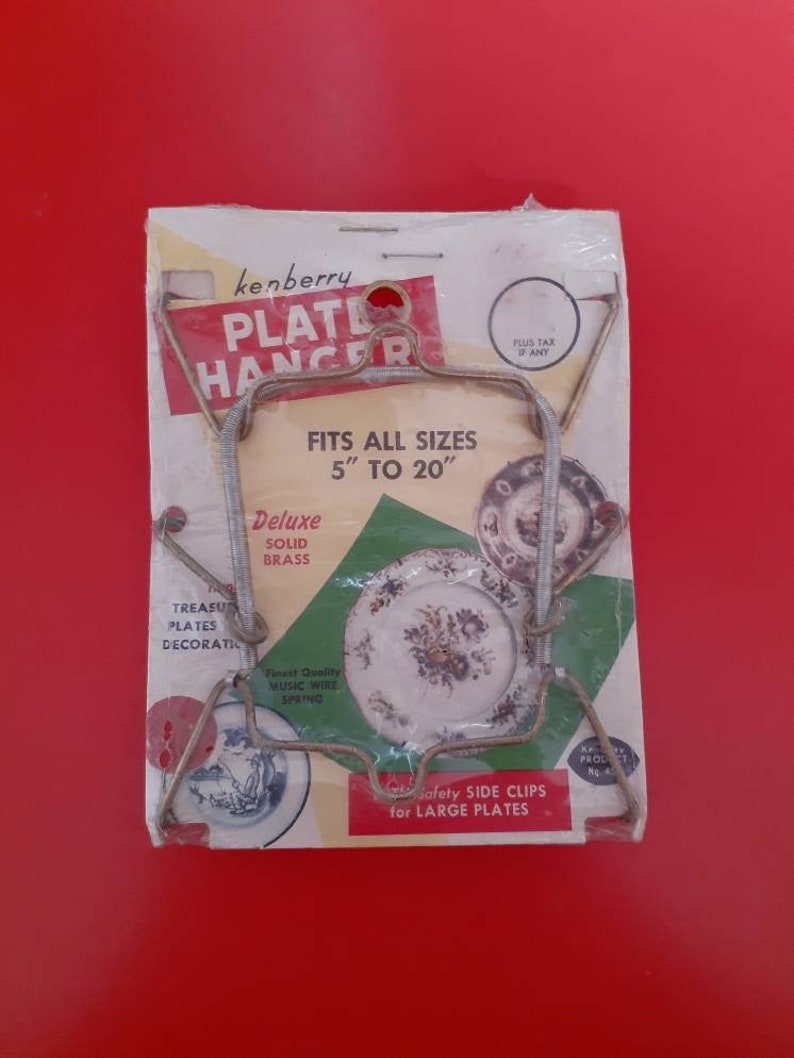 May include: A silver plate hanger with a white and green label that reads "kenberry Plate Hanger" and "Fits all sizes 5" to 20". Deluxe Solid Brass. Finest Quality Music Wire Spring. Safety Side Clips for Large Plates."