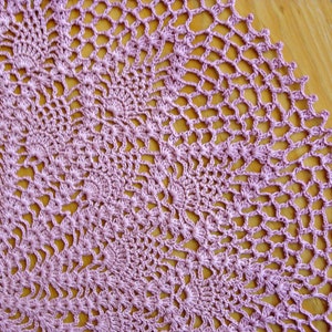 May include: A close-up of a delicate, crocheted doily in a soft lavender color. The doily is made with intricate stitches and has a circular shape.