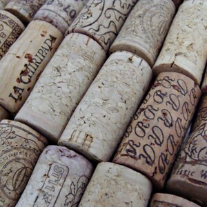 May include: A close-up of a collection of wine corks with various labels and designs. The corks are made of natural cork and have a variety of colors and textures. Some of the corks have text on them, including "LA CHIRIPADA", "BOGLE", "CONCHAY TORO", and "ST11".
